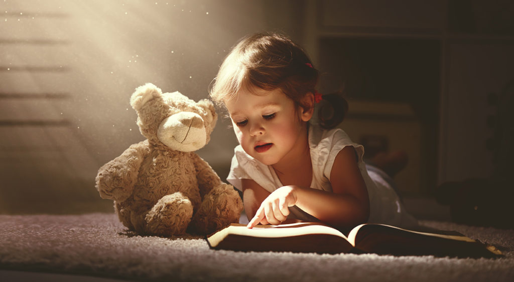 young child reading with teddy bear soft toy