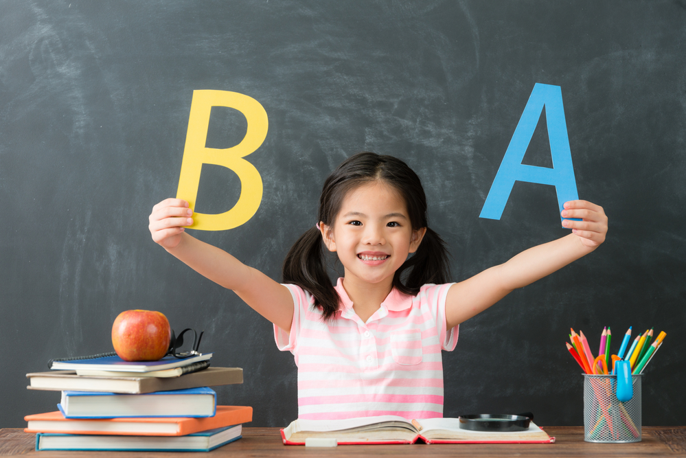 young girl student holding alphabets A and B at teacher's desk