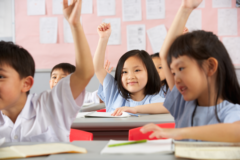 young children students raising hands in classroom