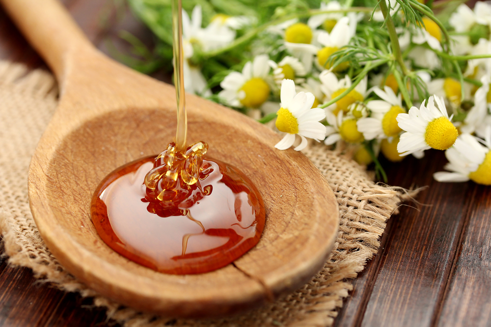 manuka honey in wooden spoon with flowers