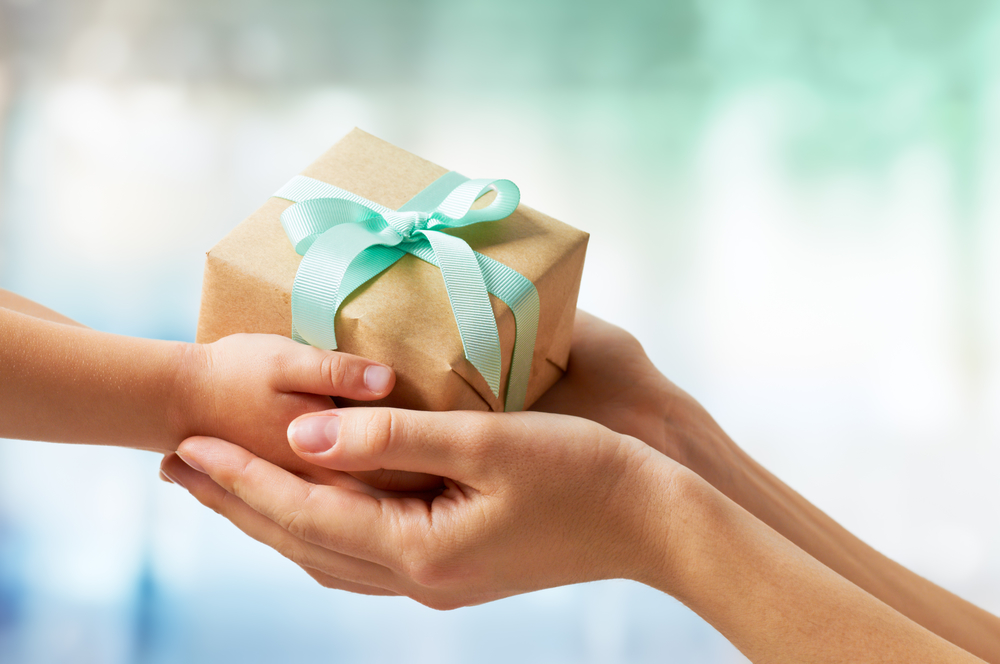 gift present box with blue bow in small hands, cupped by larger hands