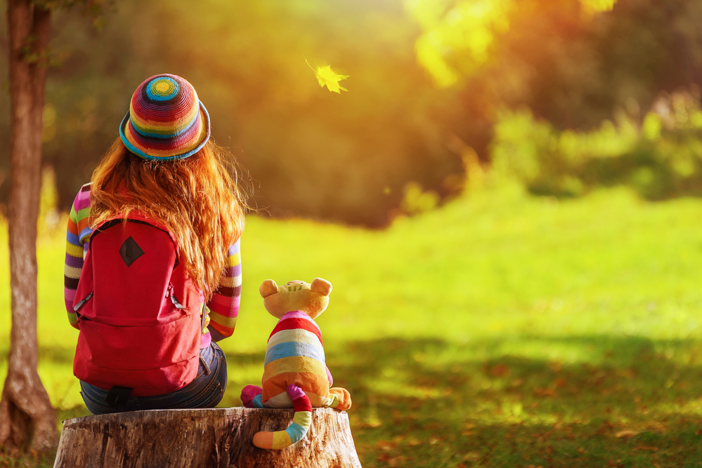child sitting with soft toy in a nature park
